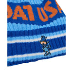 Close-up of a blue and light blue striped knit beanie with orange lettering and a small embroidered goat cartoon character on the side.