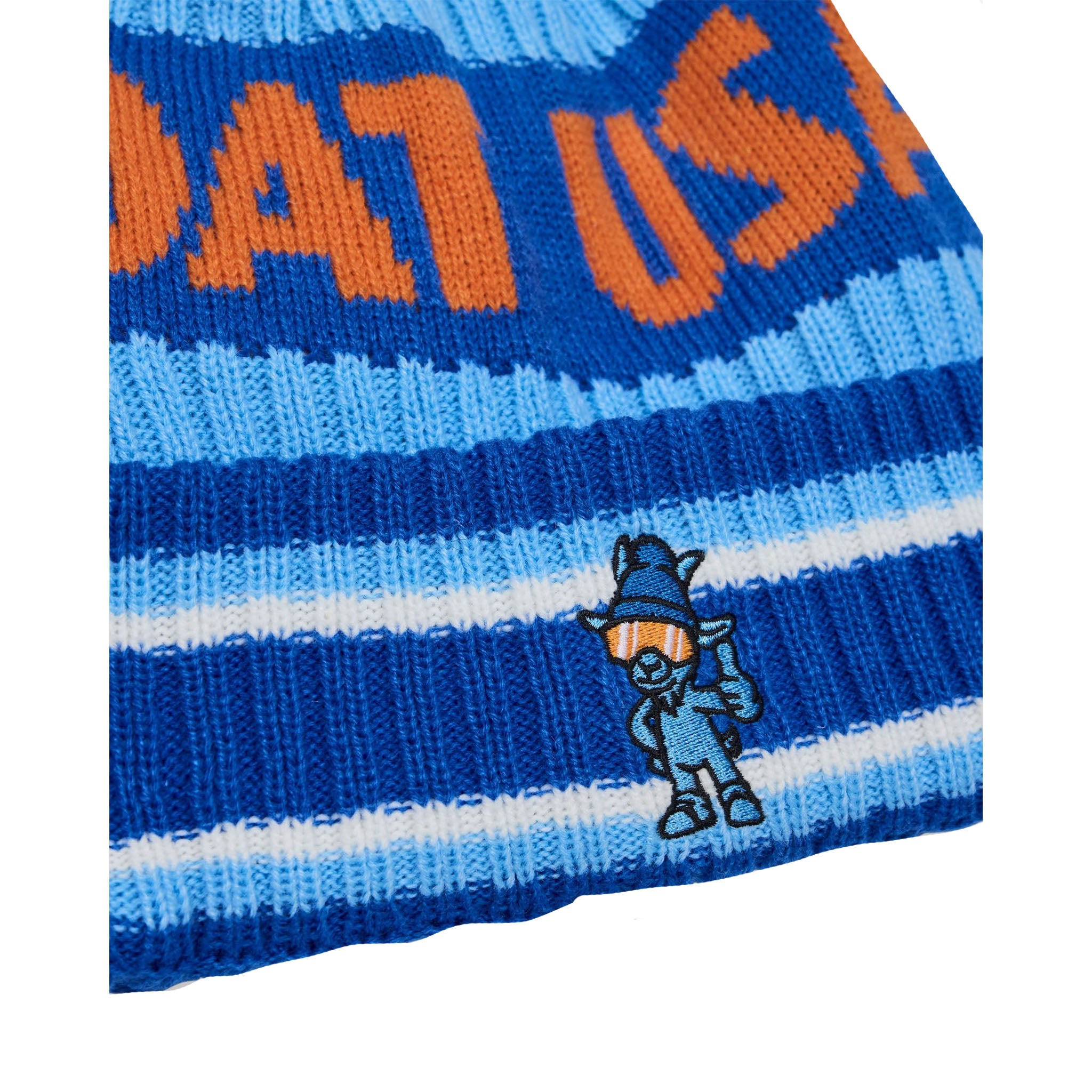 Close-up of a blue and light blue striped knit beanie with orange lettering and a small embroidered goat cartoon character on the side.