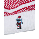Close-up of a white knit beanie with red and white patterned stripes near the top and a small goat embroidered cartoon character wearing a Santa hat on the lower cuff.