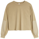 A cropped long-sleeve sweatshirt in a warm tan/beige color, featuring solid fabric on the body and contrasting slightly lighter beige patch pockets on the sleeves, shown against a plain white background.