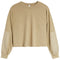 A cropped long-sleeve sweatshirt in a warm tan/beige color, featuring solid fabric on the body and contrasting slightly lighter beige patch pockets on the sleeves, shown against a plain white background.