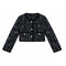 A cropped tweed jacket with long sleeves, featuring a black and white textured weave, a round neckline, three silver-tone buttons, and two front flap pockets with decorative buttons.