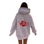 A person viewed from the back wearing an oversized light heather gray hoodie with a large red and pink hibiscus flower graphic across the back, against a plain white background.