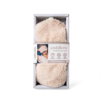 A packaged fluffy cream-colored heated eye mask, shown inside its light gray cardboard box with a paper band label.