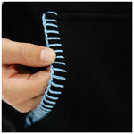 A close-up of a hand holding the edge of a black garment to show light blue contrast stitching.