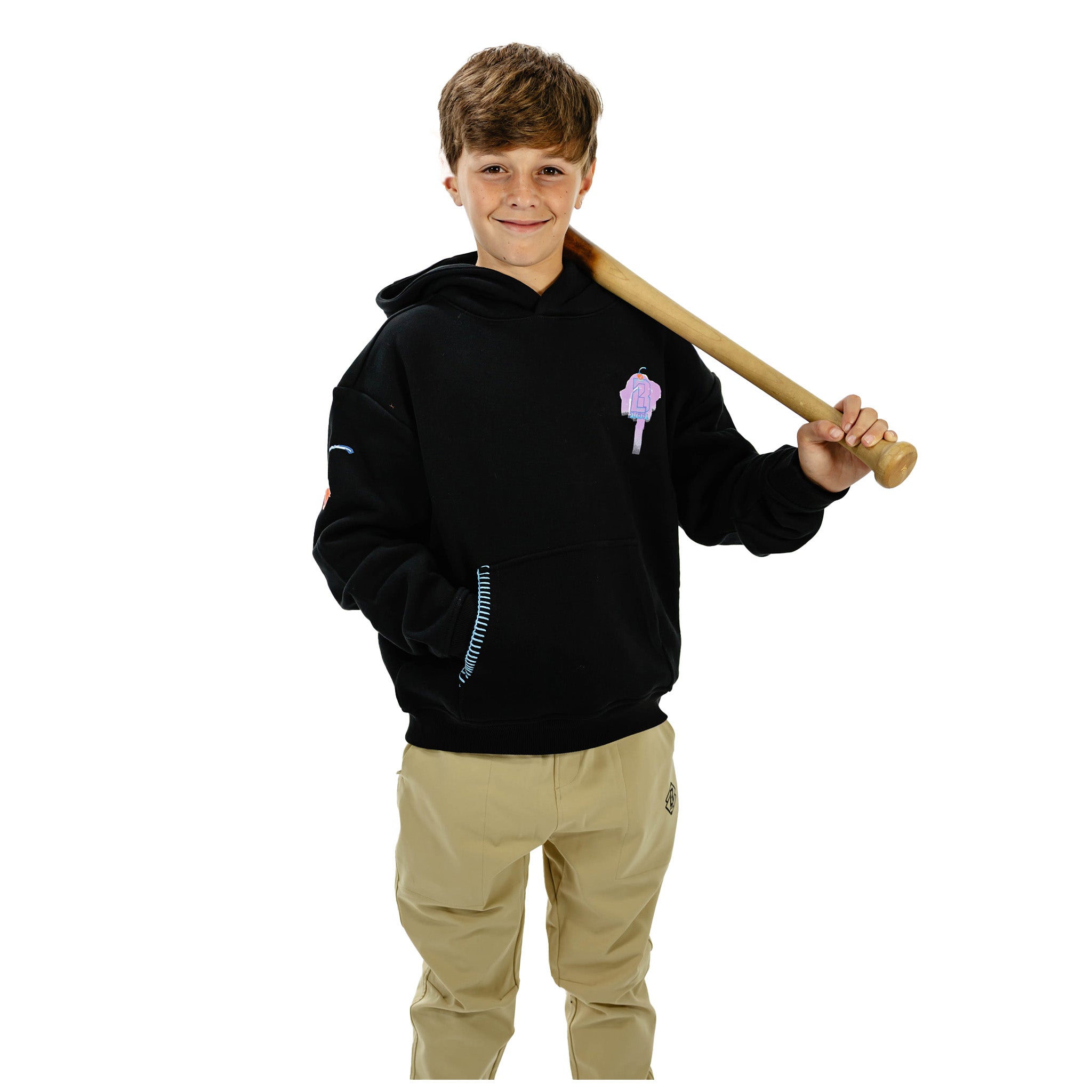 A young boy modeling a black hoodie with a small purple ice cream cone graphic on the left chest, paired with khaki pants and holding a wooden baseball bat over his shoulder against a white background.