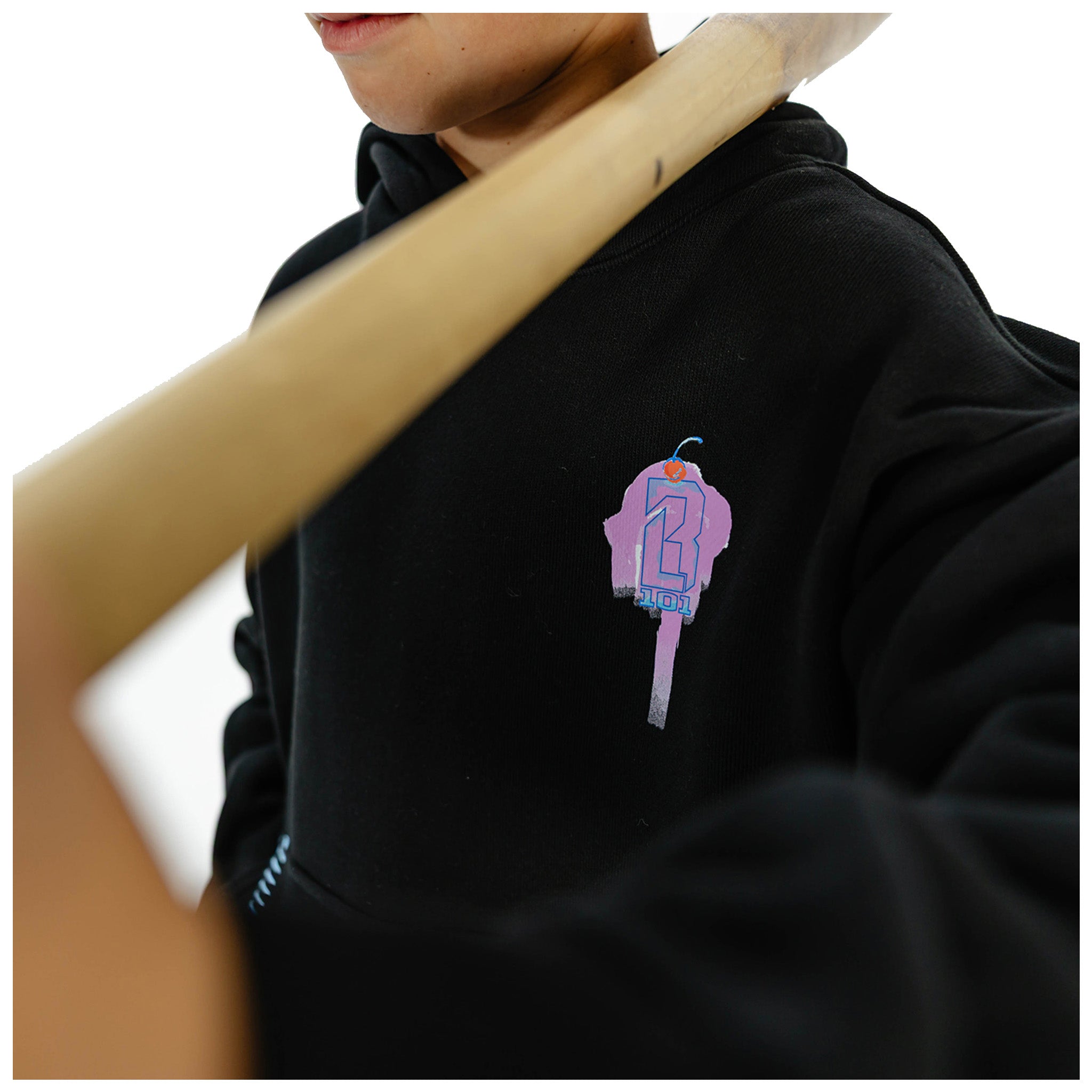 A close-up of a person wearing a black hoodie with a colorful graphic on the chest, holding a wooden pole against their shoulder.