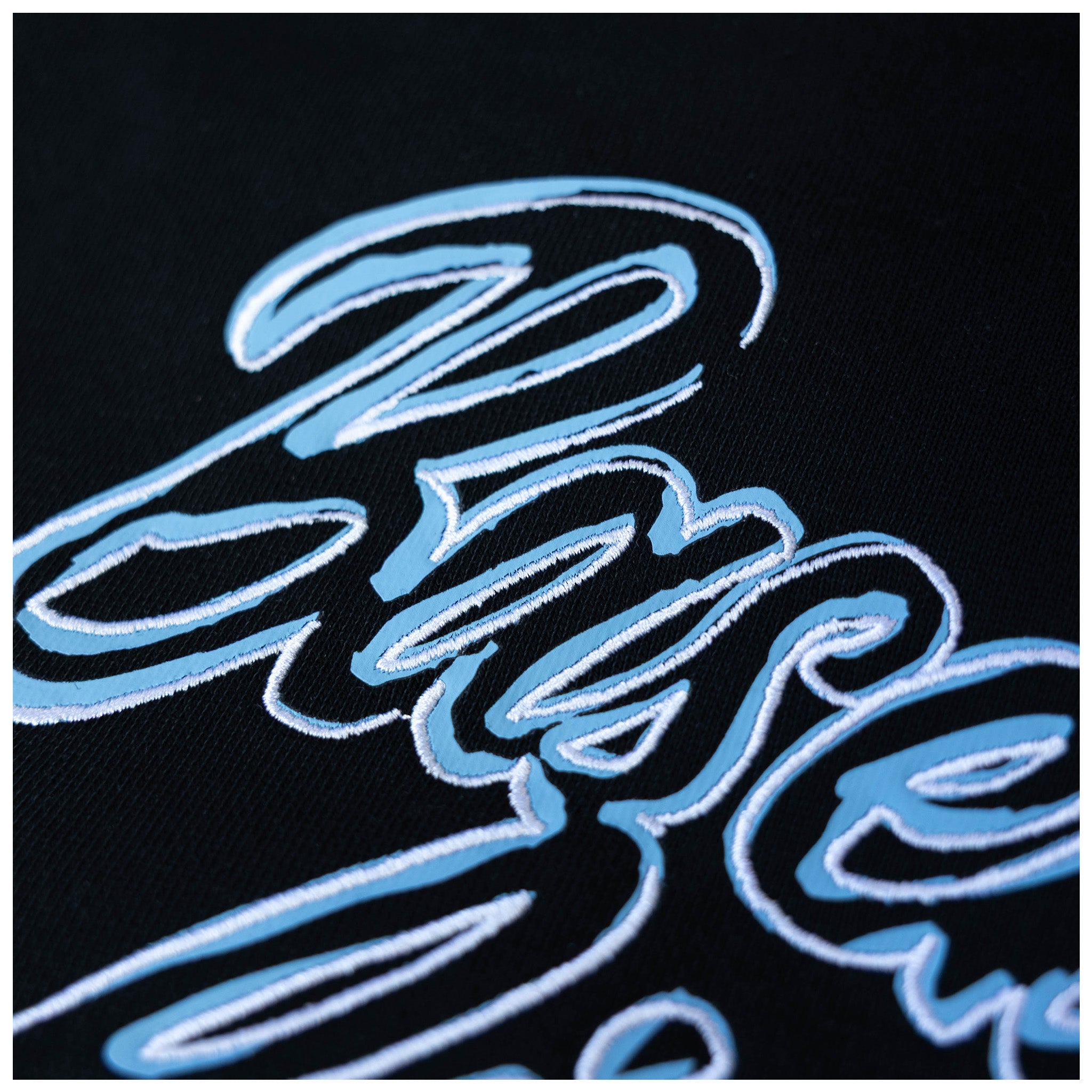 Close-up of a black fabric surface with large stylized embroidered script in light blue and white