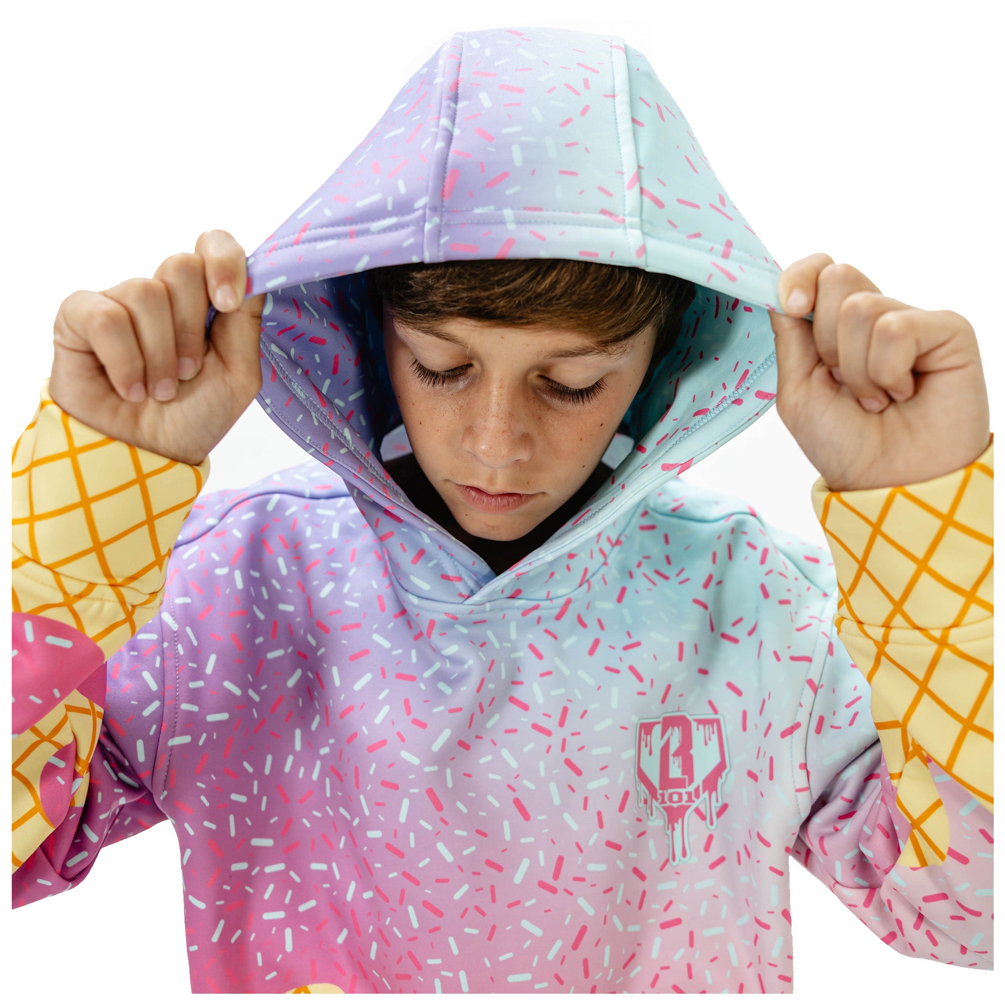 A child wearing a pastel gradient hoodie with a sprinkle pattern, holding up the hood. The hoodie features a light blue and pink gradient with white and pink sprinkles, and yellow grid-patterned sleeves.