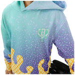 A close-up of a hooded sweatshirt with a mint-to-purple sprinkle-pattern gradient and yellow waffle-like accents near the hem, shown on a person against a white background.