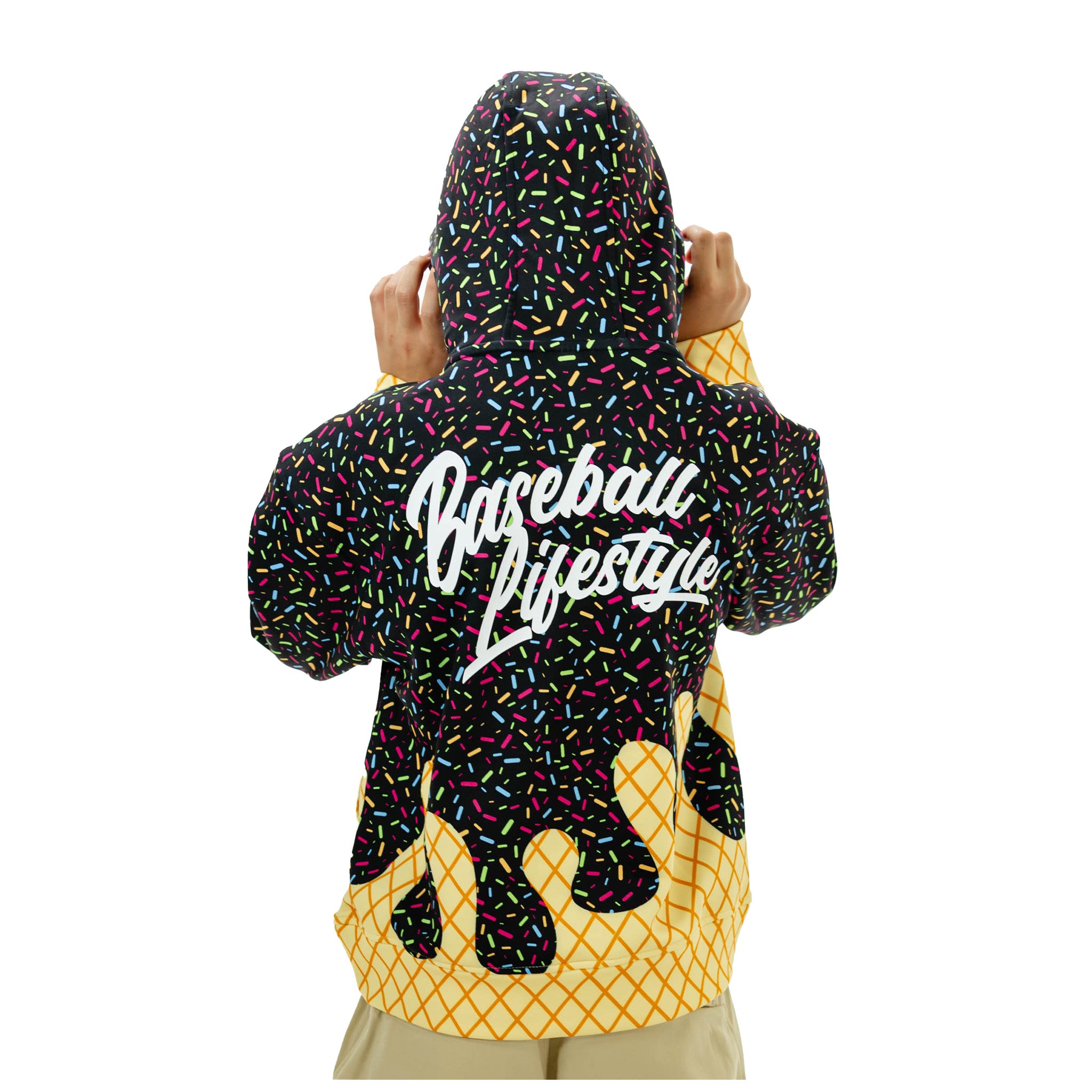 A person shown from the back wearing a hooded sweatshirt with a black sprinkle-pattern upper section, a large white 'Baseball Lifestyle' script across the back, and a yellow waffle-grid lower section resembling ice cream drips, on a plain white background.