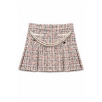 A pleated tweed mini skirt in a pink, beige, and black micro-tweed pattern, featuring a decorative cream-colored faux pearl strap across the front waistband, shown flat on a white background.