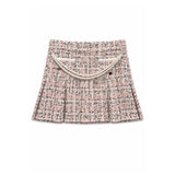 A pleated tweed mini skirt in a pink, beige, and black micro-tweed pattern, featuring a decorative cream-colored faux pearl strap across the front waistband, shown flat on a white background.