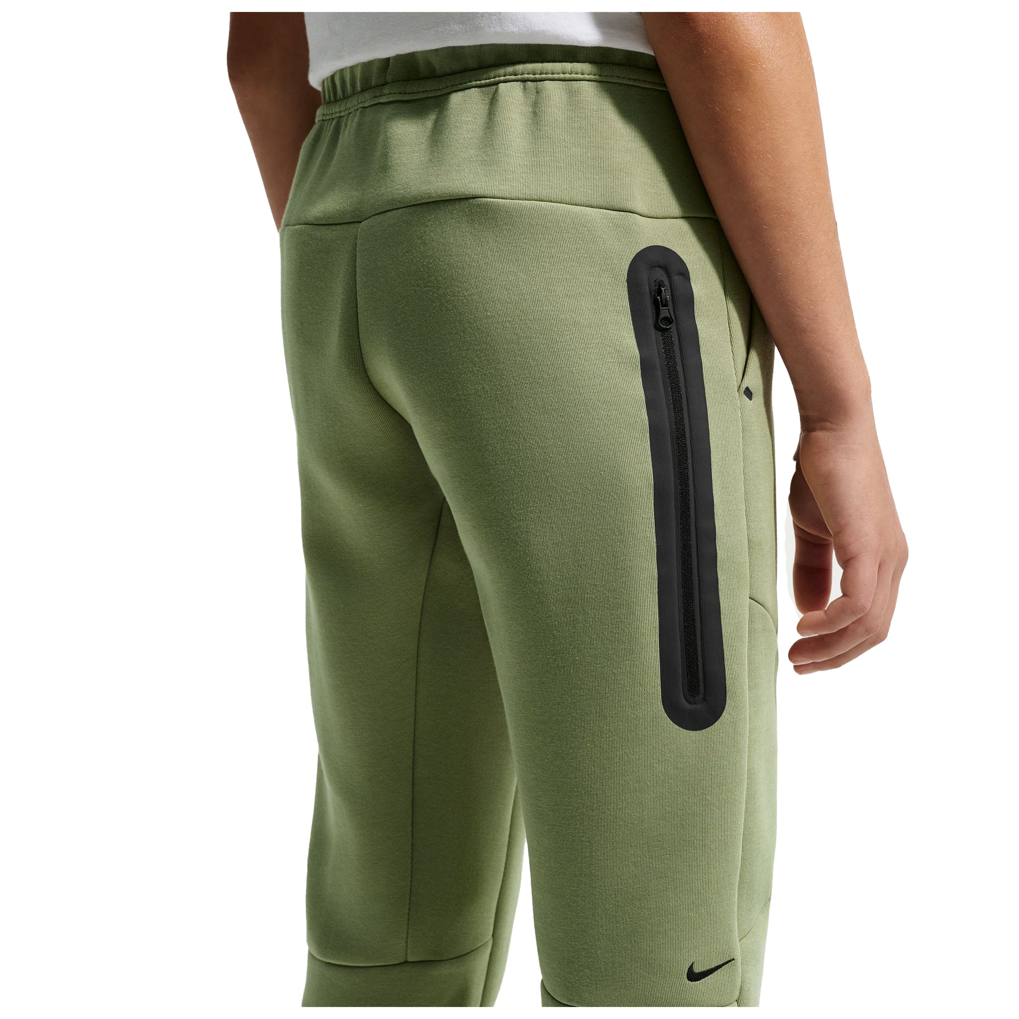 A close-up of a person wearing sage green Nike fleece jogger pants, showing the back pocket with a vertical black zippered pocket and a small black Nike swoosh near the lower leg.