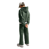 A child shown from the back wearing a dark green cropped hoodie and matching sweatpants, a white baseball cap, and white sneakers, against a plain white background.