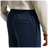 Close-up of a person wearing navy blue sweatpants with an elastic waistband and a welt pocket on the back, paired with a cream patterned long-sleeve top.