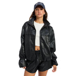 A model wearing a black faux-leather zip-up jacket with flap chest pockets, styled with black shorts, a white crop top, and a navy blue baseball cap with white text, set against a plain white background.