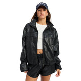 A model wearing a black faux-leather zip-up jacket with flap chest pockets, styled with black shorts, a white crop top, and a navy blue baseball cap with white text, set against a plain white background.