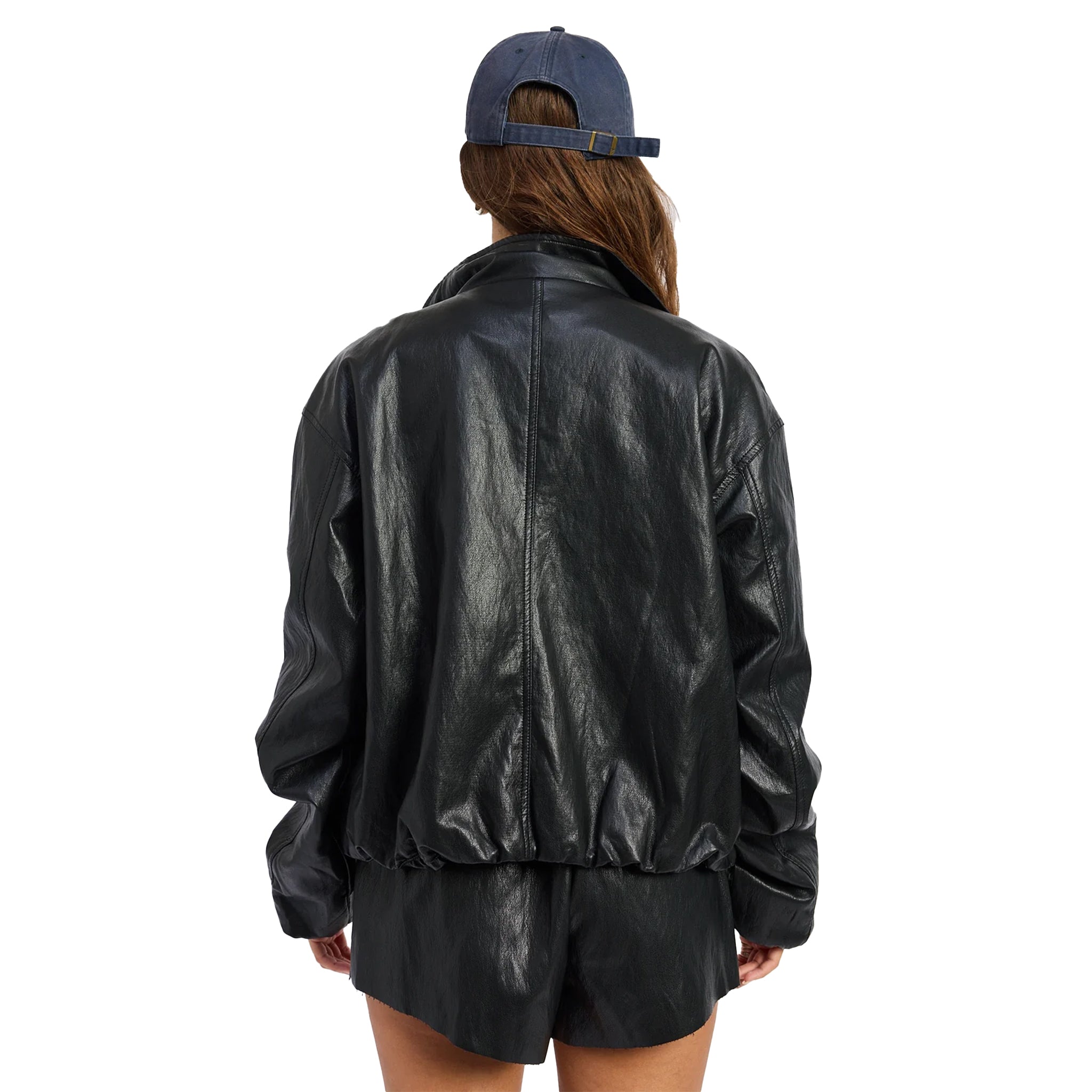 A person shown from the back wearing a black faux-leather jacket, black shorts, and a blue baseball cap against a plain white background.