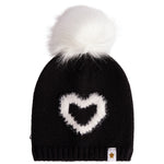 A black knit beanie hat featuring a fluffy white faux-fur pom-pom on top and a white heart-shaped knit motif on the front. A small white fabric tag with a gold star logo is visible on the lower right edge.