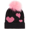 A black knit beanie hat featuring a fluffy light pink pom-pom on top and three glittery pink heart motifs on the front, set against a plain white background.