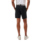 Rear view of a man wearing black athletic shorts, a white shirt, and white sneakers against a plain white background.