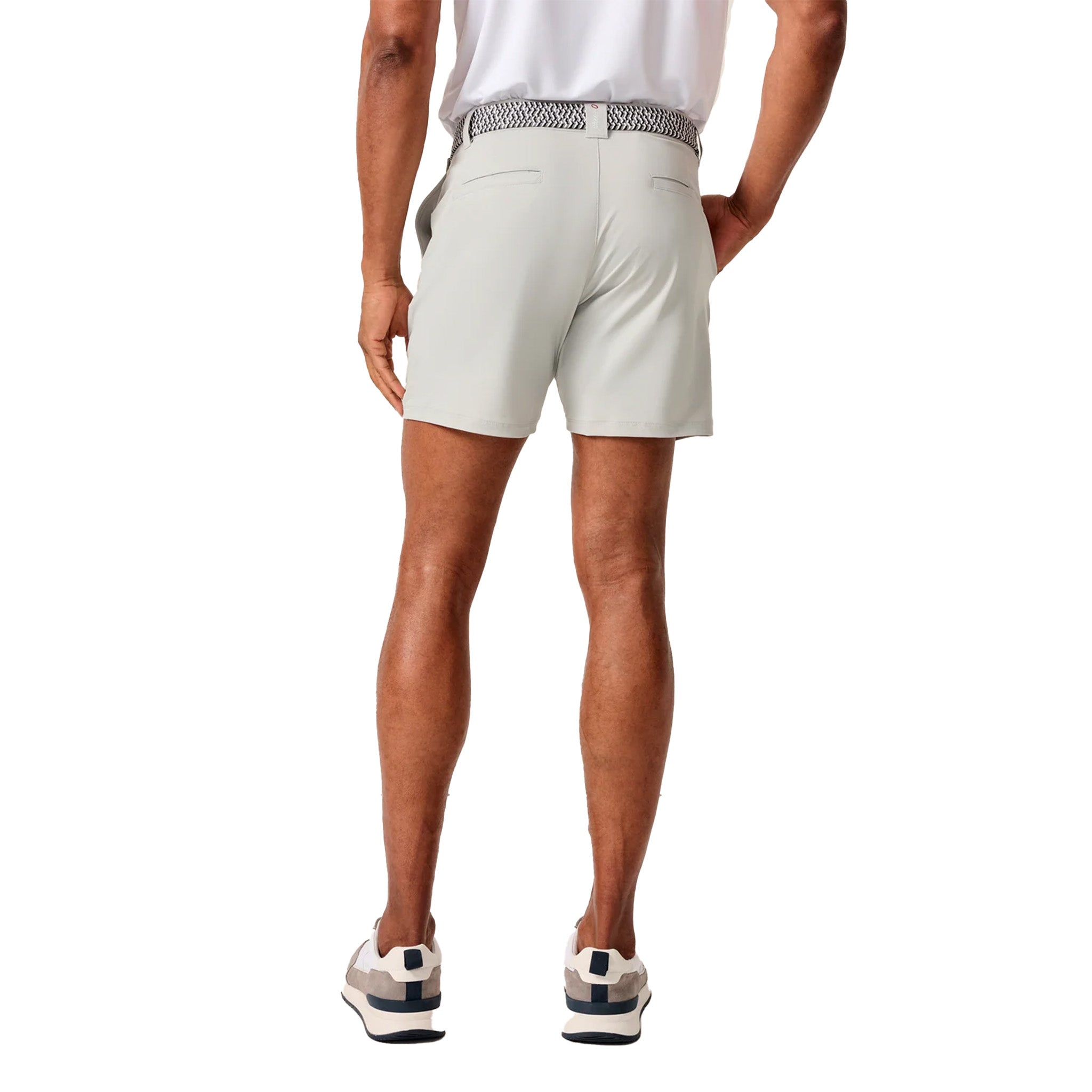 A man shown from the back wearing light beige golf shorts, a white polo shirt, and golf shoes against a solid white background.