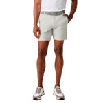 A man modeling light gray golf shorts with a patterned belt, paired with a white polo shirt and athletic sneakers, shown against a plain white background.