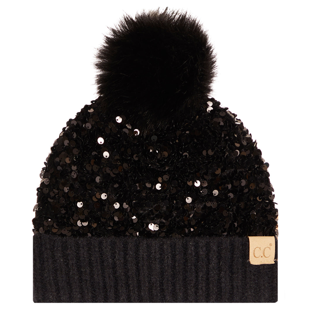 A black beanie hat with a large black faux fur pom-pom on top, covered in black sequins, featuring a ribbed knit cuff and a small tan 'cc' logo patch on the side.