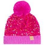 A bright pink beanie hat covered in sequins, featuring a fluffy pink pom-pom on top and a ribbed knit cuff with a small tan 'cc' logo patch.