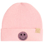 A light pink ribbed knit beanie hat for kids, featuring a black and pink rhinestone smiley face patch on the front cuff and a small tan brand tag on the side.