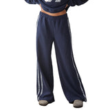 A person wearing loose navy wide-leg sweatpants with lace side stripes shown against a plain white studio background.