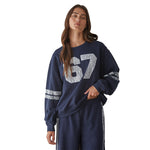 A woman modeling a navy blue sweatshirt. The sweatshirt features a large textured lace '67' graphic on the front and lace stripes on the sleeves, paired with matching navy pants that have lace side stripes.