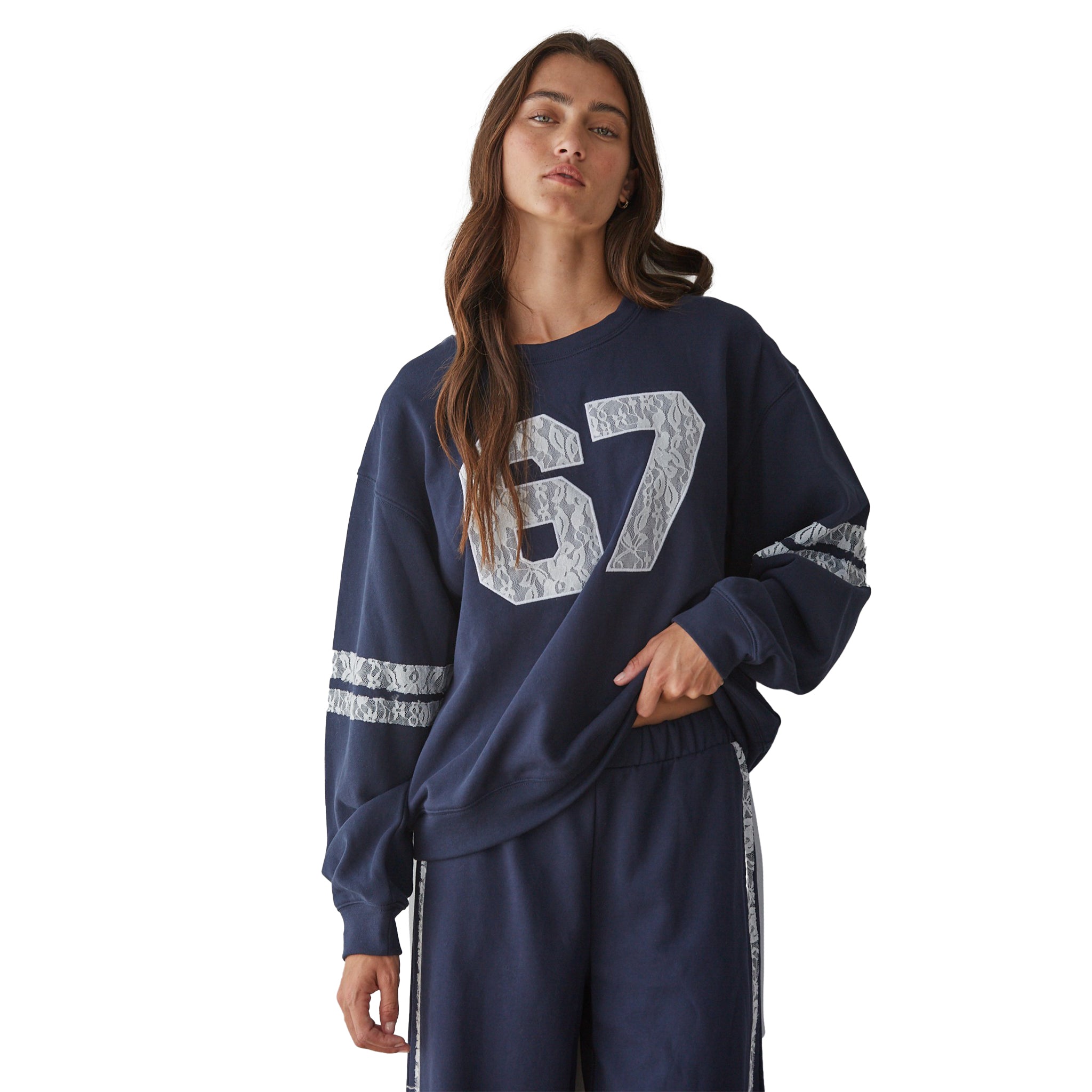A woman modeling a navy blue sweatshirt. The sweatshirt features a large textured lace '67' graphic on the front and lace stripes on the sleeves, paired with matching navy pants that have lace side stripes.