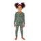 A young girl with dark curly hair in pigtails wearing a green long-sleeve pajama set with a pink and white floral pattern, standing against a solid white background.