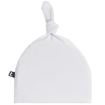 A white ribbed muslin baby hat with a knotted top and a small black fabric brand tag on the side, shown against a plain white background.