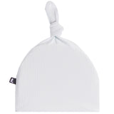 A white ribbed muslin baby hat with a knotted top and a small black fabric brand tag on the side, shown against a plain white background.
