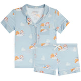 A two-piece children's pajama set in light blue, featuring a short-sleeve button-front top with a chest pocket and matching shorts. The fabric has an all-over print cappuccino with white piping details.