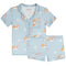 A two-piece children's pajama set in light blue, featuring a short-sleeve button-front top with a chest pocket and matching shorts. The fabric has an all-over print cappuccino with white piping details.