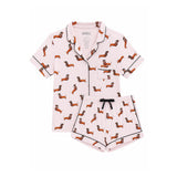A two-piece women's pajama set featuring a short-sleeve button-front top and matching shorts in light pink, printed with an all-over dachshund pattern and finished with black piping and a black drawstring.