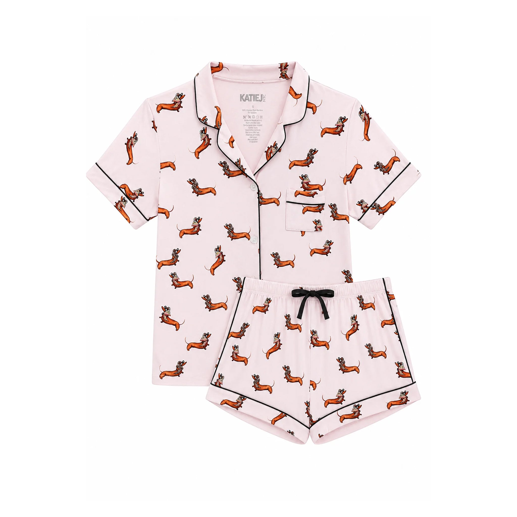 A two-piece women's pajama set featuring a short-sleeve button-front top and matching shorts in light pink, printed with an all-over dachshund pattern and finished with black piping and a black drawstring.