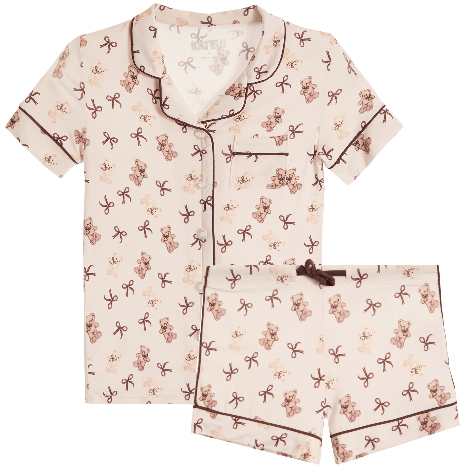 A two-piece short-sleeve pajama set featuring a cream-colored fabric with an all-over teddy bear and bow print, complete with dark brown piping and a matching drawstring tie on the shorts.