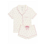 A two-piece pajama set featuring a short-sleeve button-front top and matching shorts in an off-white base with a small pink and blue ballerina print, finished with pink piping and a pink drawstring.