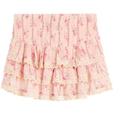 A light pink tiered skirt with a delicate floral print, featuring an elastic smocked waistband and layered ruffles finished with cream lace trim.