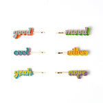 Six colorful enamel hair clips spelling out positive words: 'good', 'mood', 'cool', 'vibes', 'yeah', and 'nope'. Each clip has a gold-tone metal base with a vibrant, multicolored script font on a clean white background.