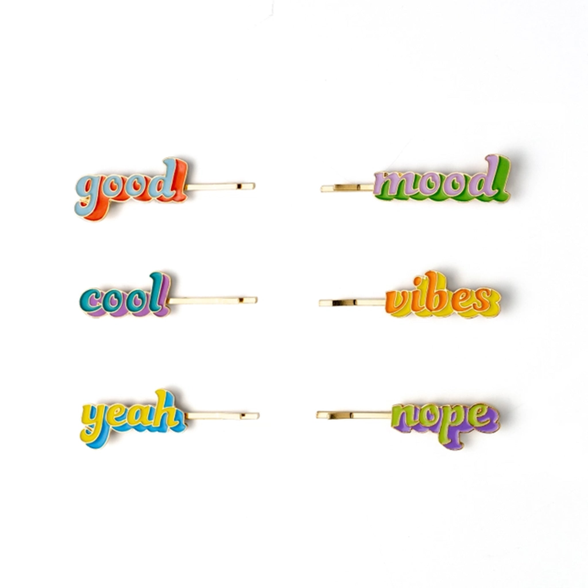 Six colorful enamel hair clips spelling out positive words: 'good', 'mood', 'cool', 'vibes', 'yeah', and 'nope'. Each clip has a gold-tone metal base with a vibrant, multicolored script font on a clean white background.