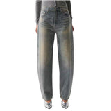 A person wearing faded gray wide-leg jeans with a subtle yellowish wash on the front, paired with a gray long-sleeve top and metallic silver pointed shoes, shown against a plain white background.