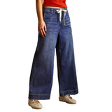 A person wearing wide-leg blue denim jeans with a cream drawstring waist, paired with a red top and beige sneakers, shown against a plain white background.