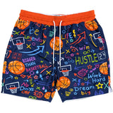 A pair of navy blue basketball shorts with a vibrant multicolor graphic print featuring basketballs, hoops, and motivational text like 'Be Legendary' and 'Hustle'. The shorts have an orange elastic waistband and white drawstrings.