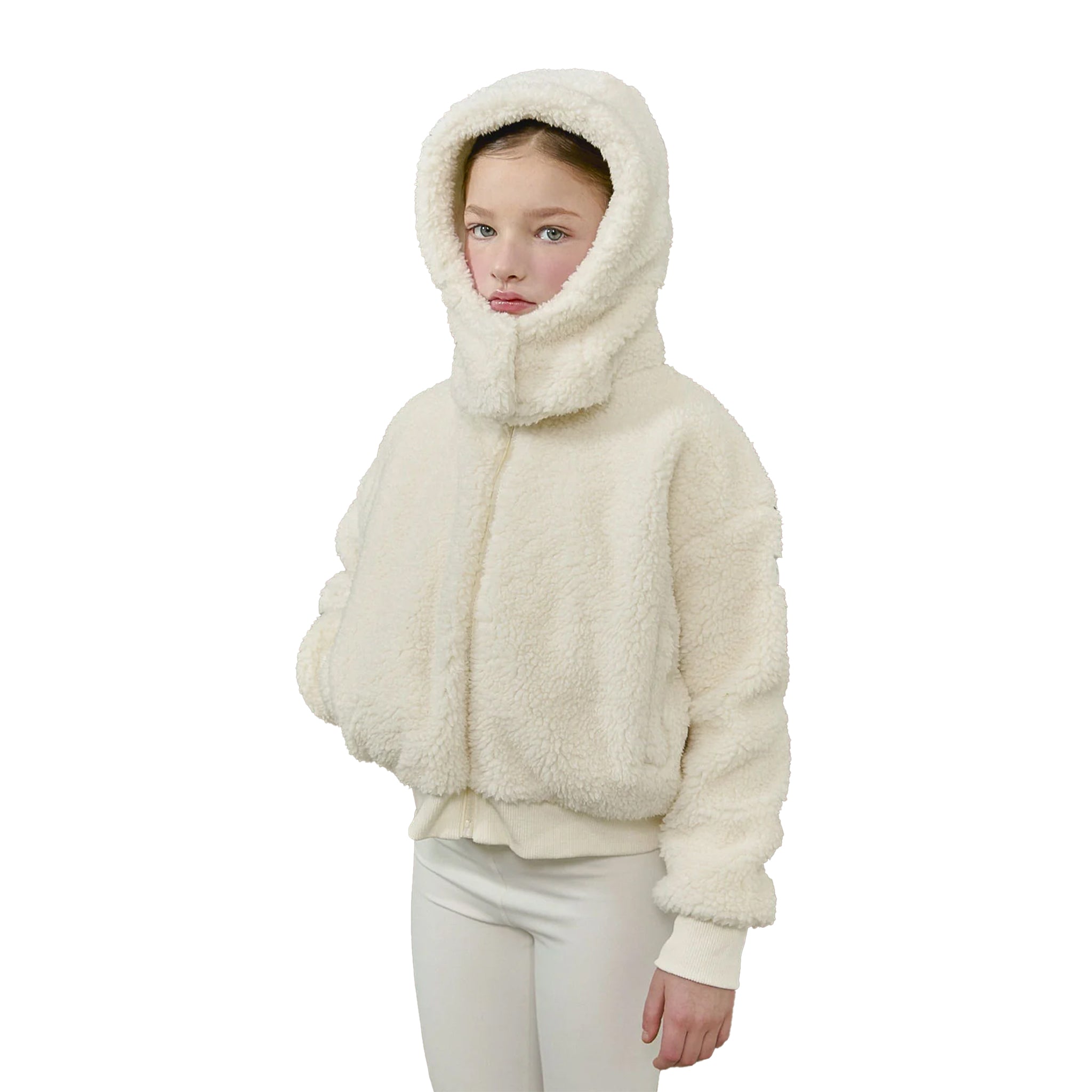 A child wearing a cream-colored sherpa fleece hooded jacket with a high collar and white pants, photographed against a solid white background.